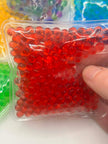Red gel beads in a clear plastic package held by a hand against a colorful background