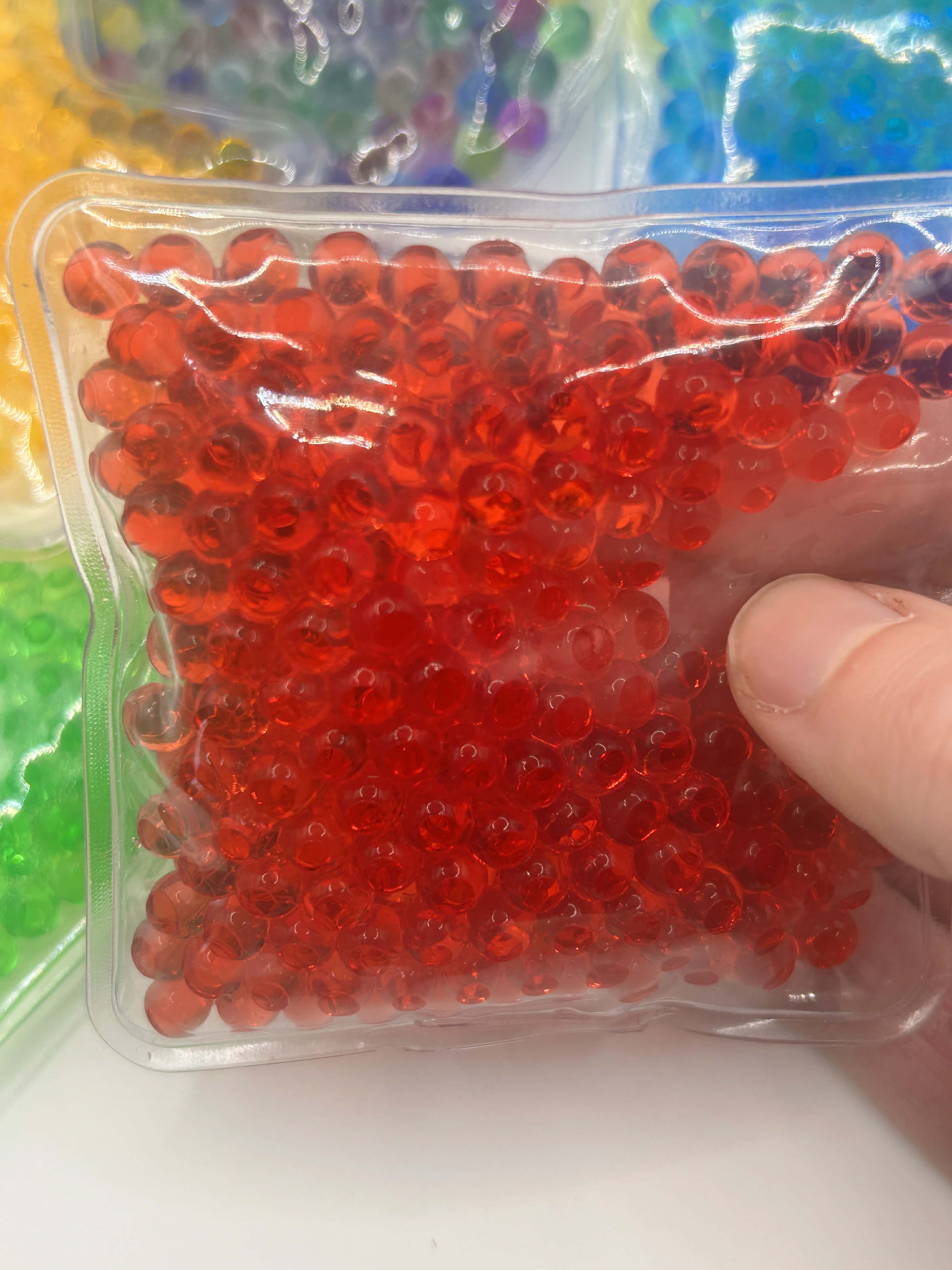 Red gel beads in a clear plastic package held by a hand against a colorful background