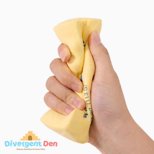 Hand holding a yellow stress butter block fidget with 'Divergent Den' logo in the corner