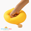 Hand squeezing a yellow stress ball with a cookie-shaped object on a white background, featuring the Divergent Den logo.
