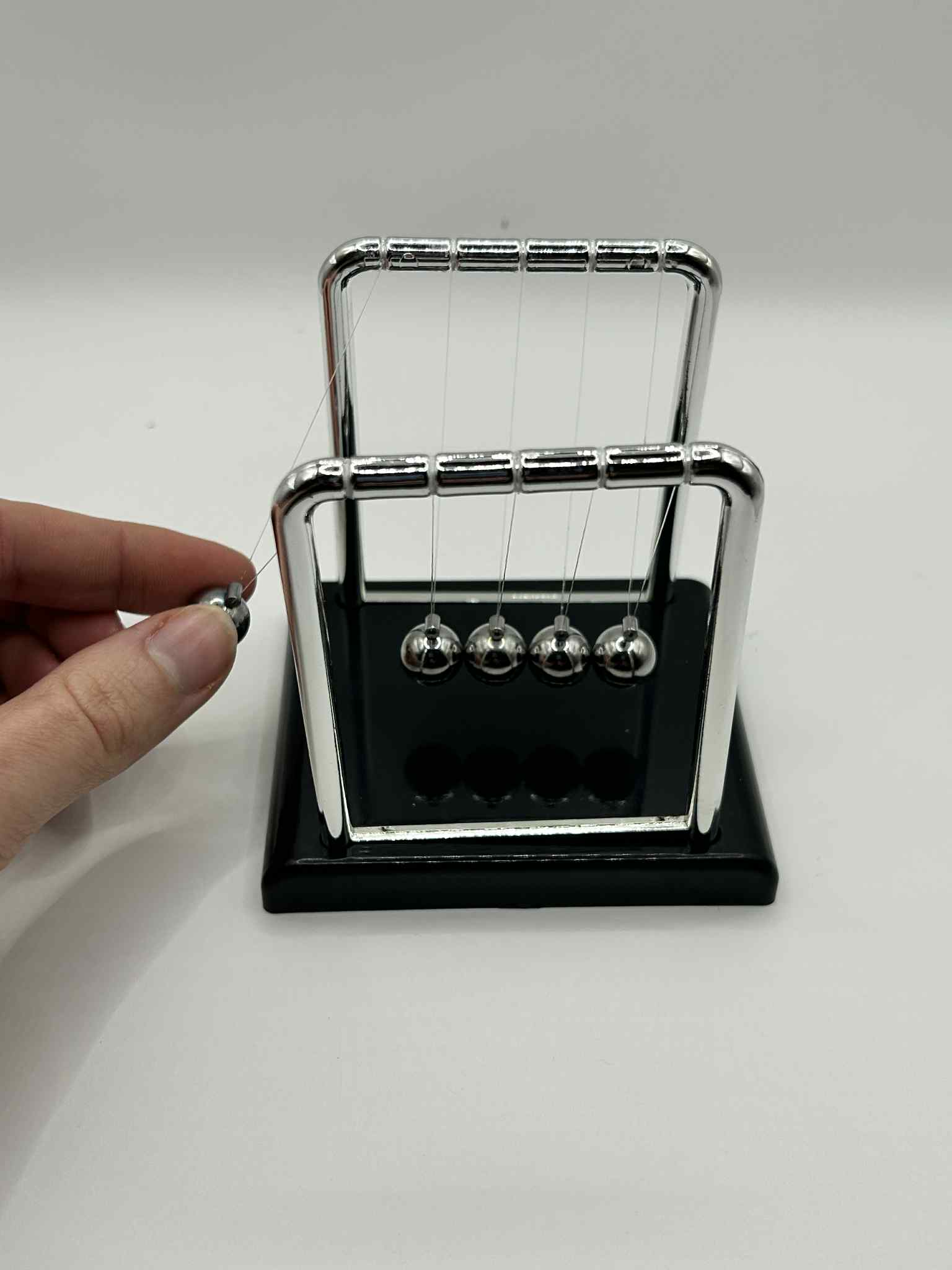 Newton’s Cradle – hand showing how we use the newtons cradle. Classic desk fidget toy for focus and stress relief | The Divergent Den