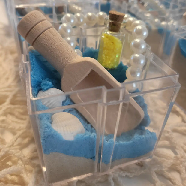 Small transparent box with blue sand, a wooden paddle, and a bottle with yellow contents on a textured surface.