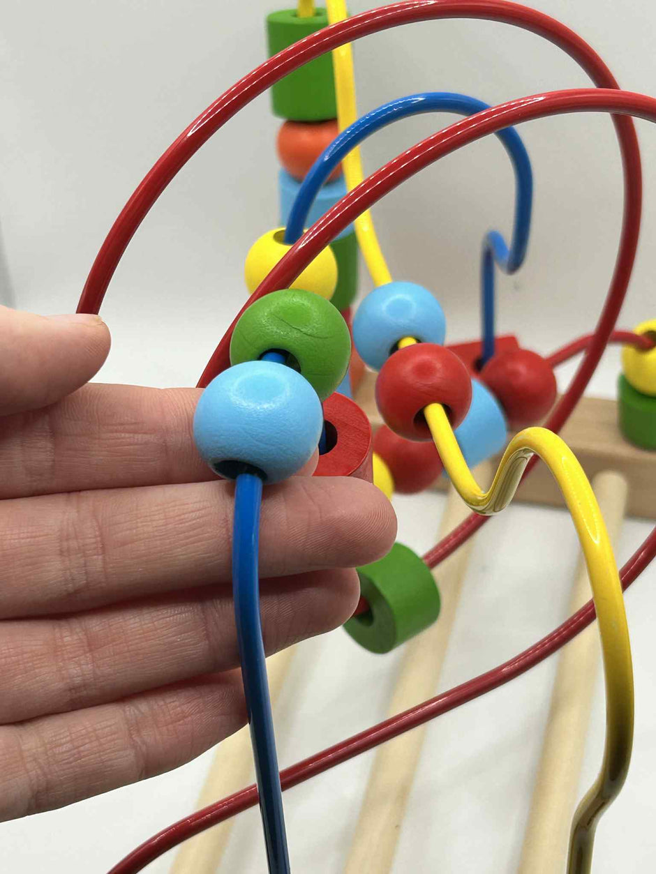 Close-up of Wooden Bead Maze alongside a hand to show the size of the beads and showing colourful wooden beads on wire tracks for tactile play