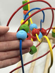 Close-up of Wooden Bead Maze alongside a hand to show the size of the beads and showing colourful wooden beads on wire tracks for tactile play