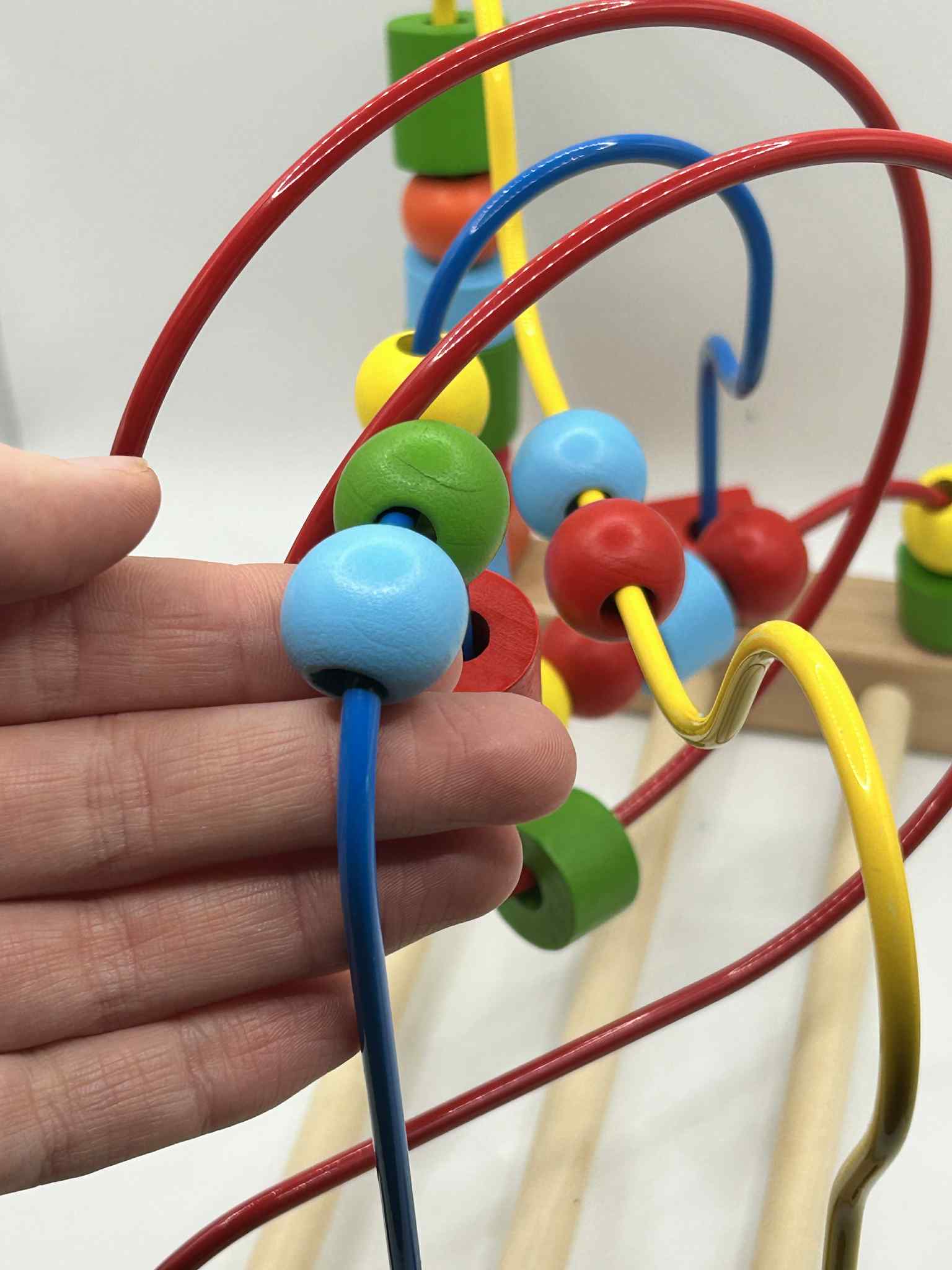 Close-up of Wooden Bead Maze alongside a hand to show the size of the beads and showing colourful wooden beads on wire tracks for tactile play